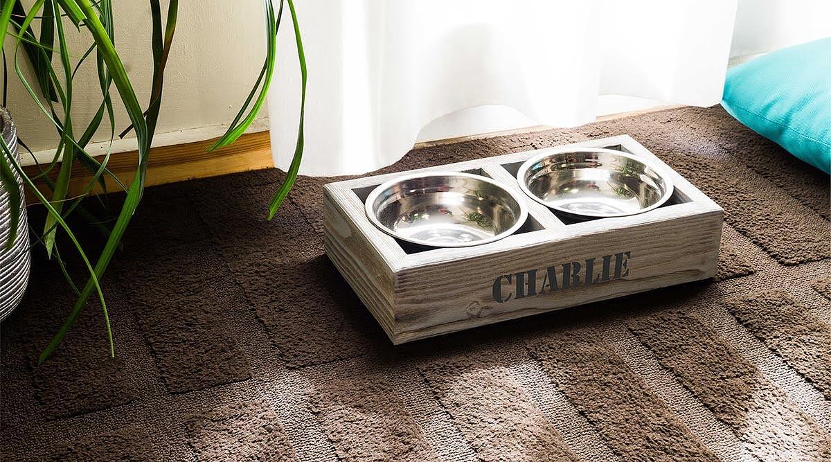 4Legs ръчно изработена стойка за купи Eki с две метални купи и дървена основа, поставена на килим.