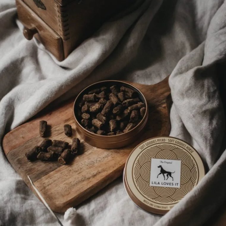 Lila Loves It soft horse meat treats in a round tin, on a wooden board with a cozy blanket.