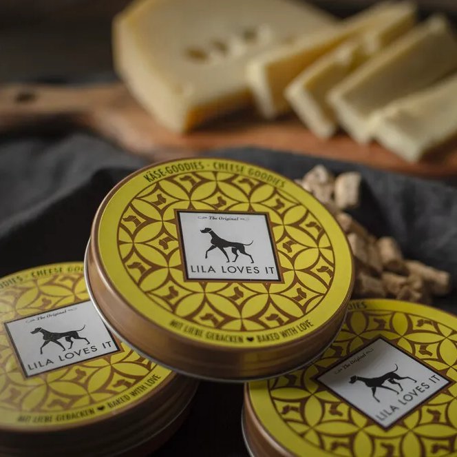 Меки лакомства със сирене Lila Loves It в опаковка, на фона на резени сирене и лакомства за кучета.