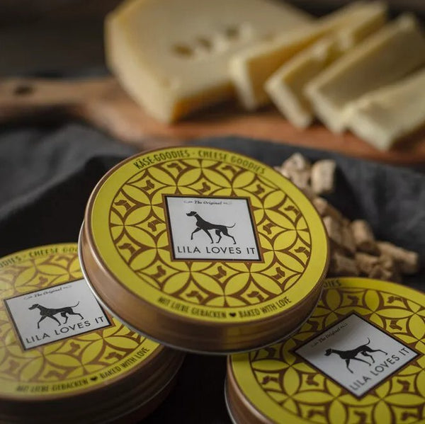 Меки лакомства със сирене Lila Loves It в опаковка, на фона на резени сирене и лакомства за кучета.